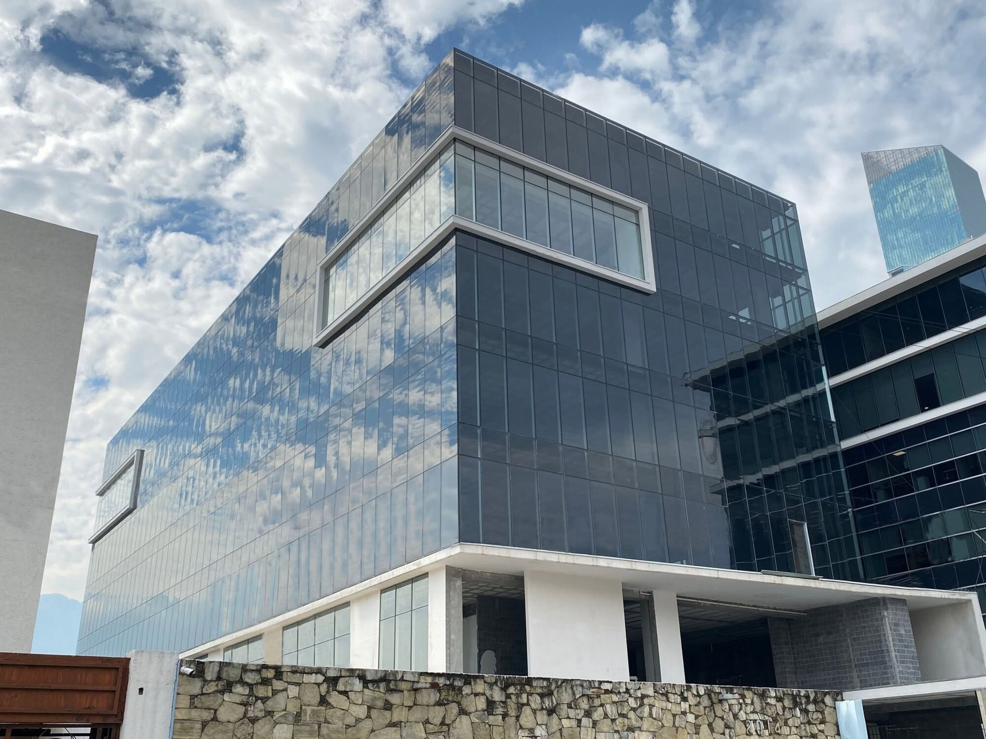 Torre Gautier: volumen de cristal oscuro con marcos blancos que sobresalen, sobre el muro de piedra de la calle